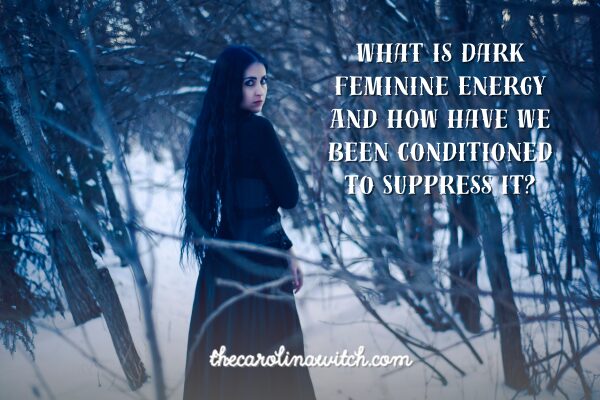 What Is Dark Feminine Energy and How Have We Been Conditioned to Suppress it? Blog post title with a picture of a woman standing on a forest path walking away from us, but turning around and looking back at us.